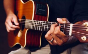 Nahaufnahme einer Akustikgitarre mit greifenden Händen am Griffbrett