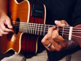 Nahaufnahme einer Akustikgitarre mit greifenden Händen am Griffbrett
